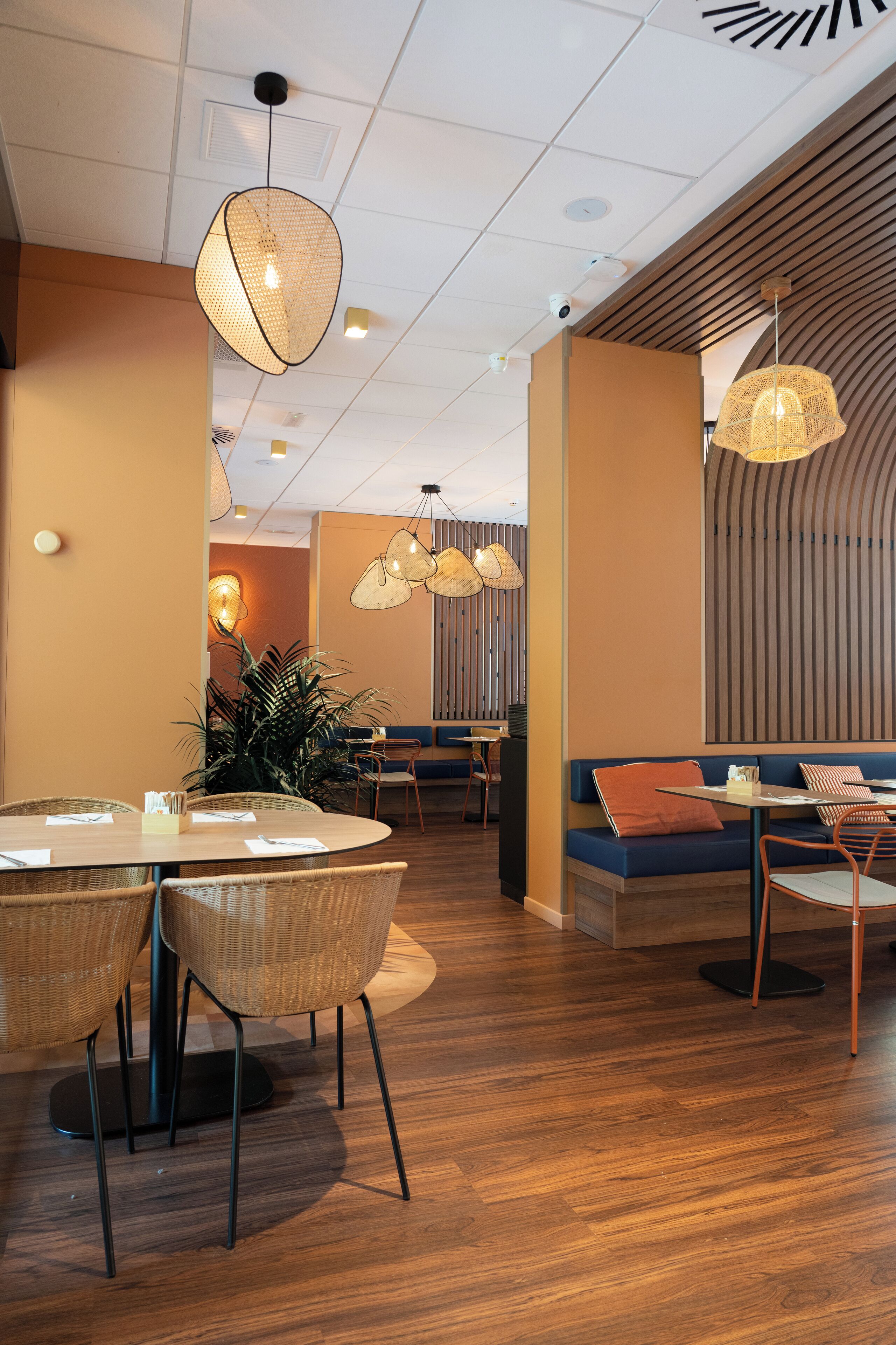 Interior moderno de restaurante con mesas redondas, sillas de mimbre y lámparas colgantes.