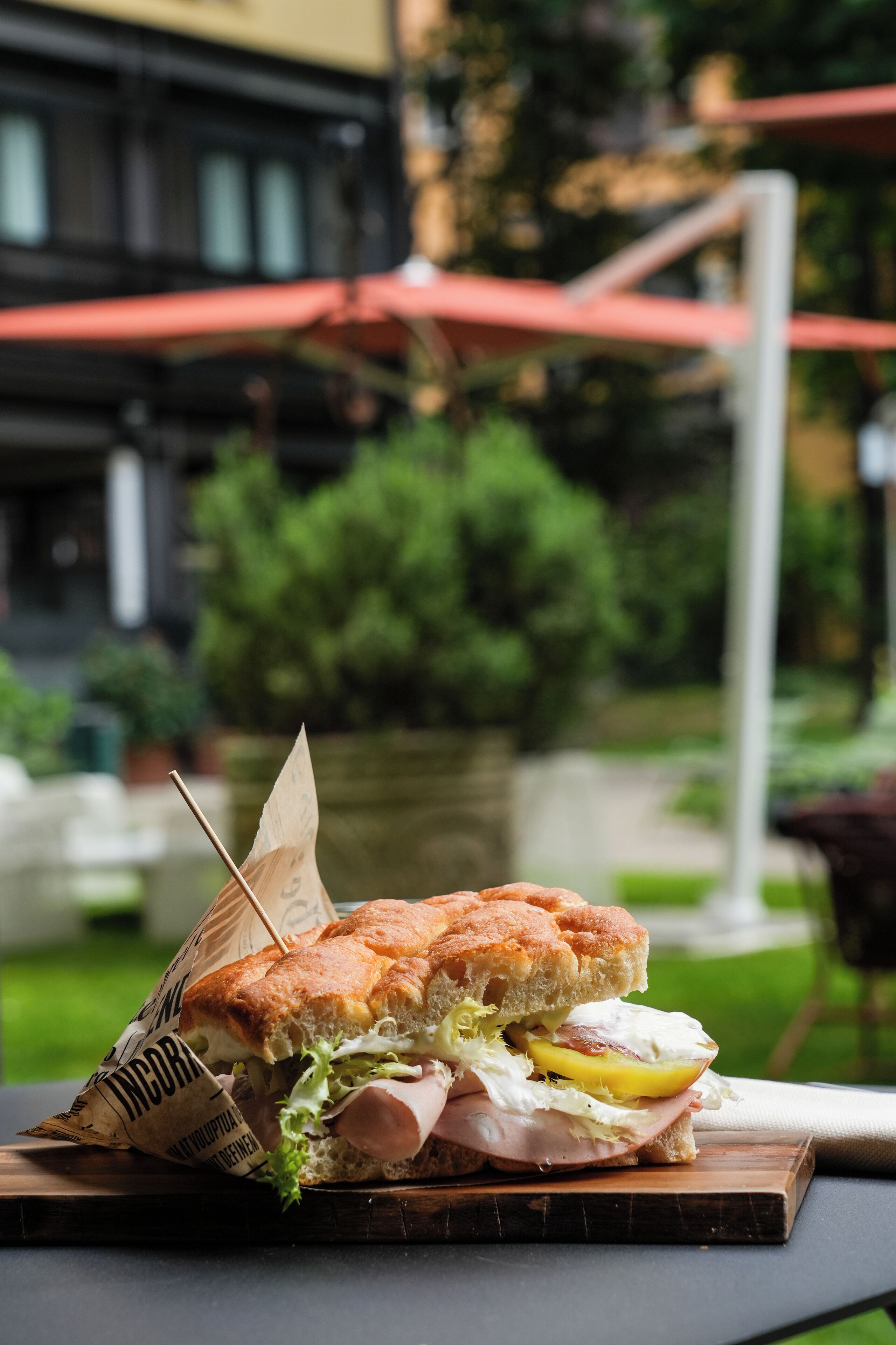 Un sándwich sobre una tabla de madera, con un fondo borroso al aire libre.