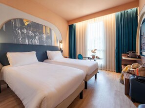 A hotel room with two beds, a desk, a chair, a table with a vase, and a suitcase. - Mercure Bologna Centro (Bologna)
