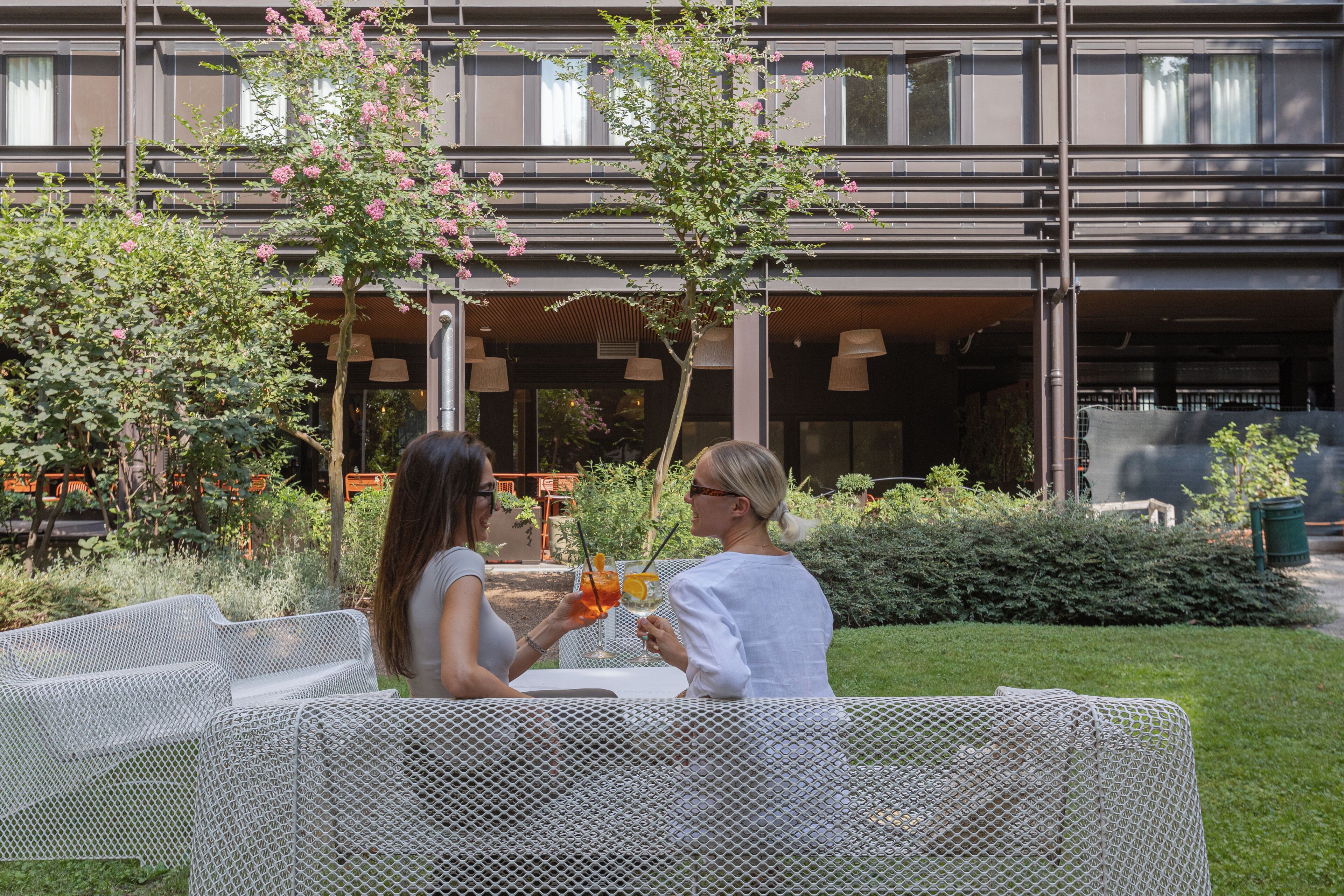 Dos personas sentadas a una mesa con vista a un edificio y vegetación al fondo.