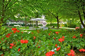 A park with a gazebo, green foliage, and red flowers. - Mercure Bologna Centro (Bologna)