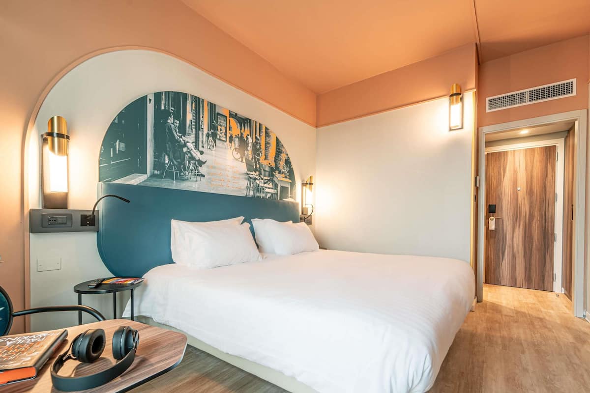 Ein Hotelzimmer mit einem großen Bett, einem Schreibtisch mit Stuhl, einem an der Wand montierten Fernseher und einer Tür mit Holzverkleidung.