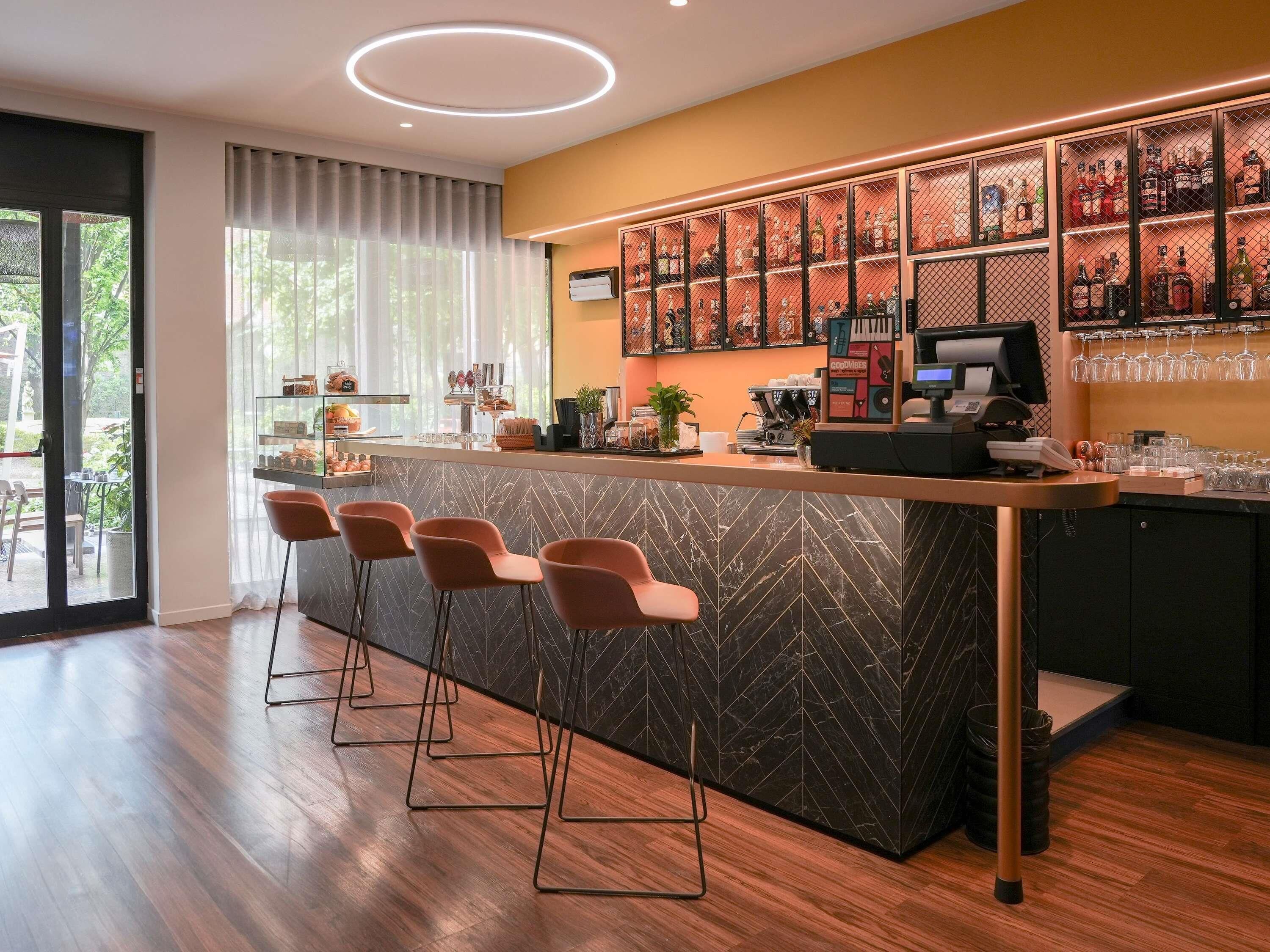 Una zona de bar moderna con mostrador, taburetes, una máquina de café y una vitrina de vidrio con botellas.