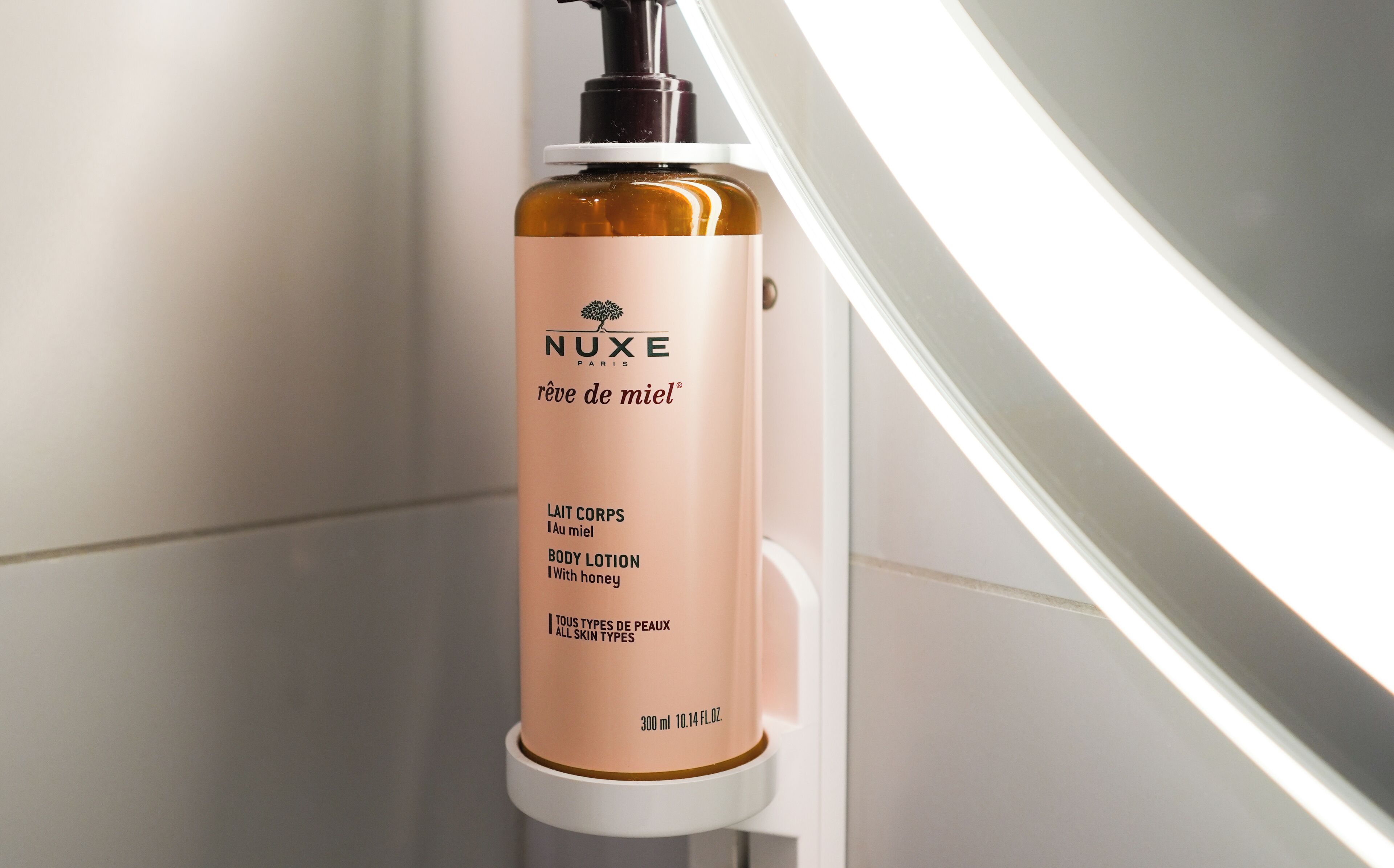 Une bouteille de lotion corporelle NUXE sur une étagère blanche.