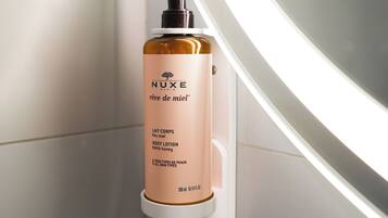 Una botella de crema corporal NUXE sobre un estante blanco.