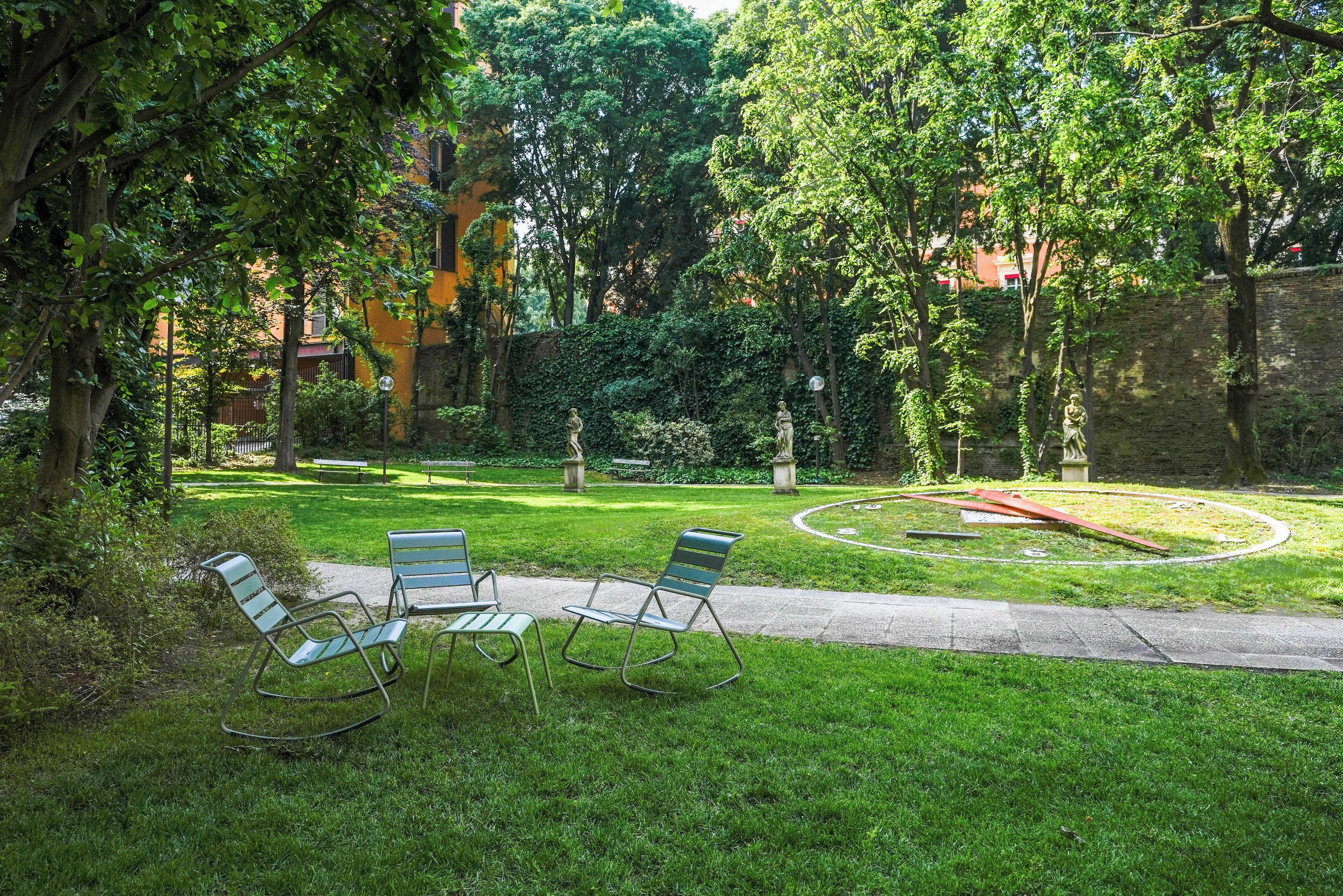 Un jardín bien cuidado con tres mecedoras, un sendero de piedra circular y una estatua al fondo.