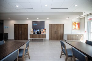 A modern meeting room with a long table, chairs, and a coffee station.