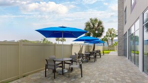 A patio area with outdoor seating and umbrellas, a stone-tiled floor, and a view of a building with large windows. - Holiday Inn Express & Suites Tampa Stadium – Airport Area by IHG (Tampa)