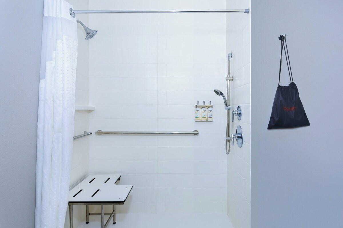 A modern bathroom with a shower, grab bars, a towel rack, and a small table.
