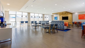 A spacious indoor area with multiple seating arrangements, including tables and chairs, and a large window providing a view outside. - Holiday Inn Express & Suites Tampa Stadium – Airport Area by IHG (Tampa)