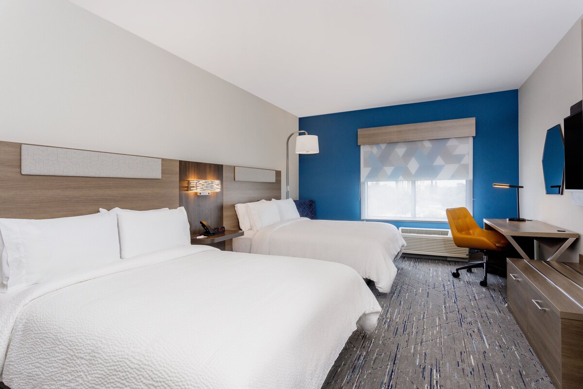 A hotel room with two beds, a desk, a chair, and a TV.