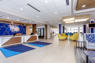 A modern hotel lobby with reception desks, seating areas, and a refreshment bar.