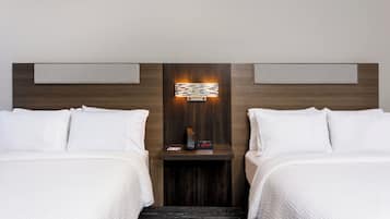 A hotel room with two beds, a nightstand, a wall-mounted light, and a digital clock.