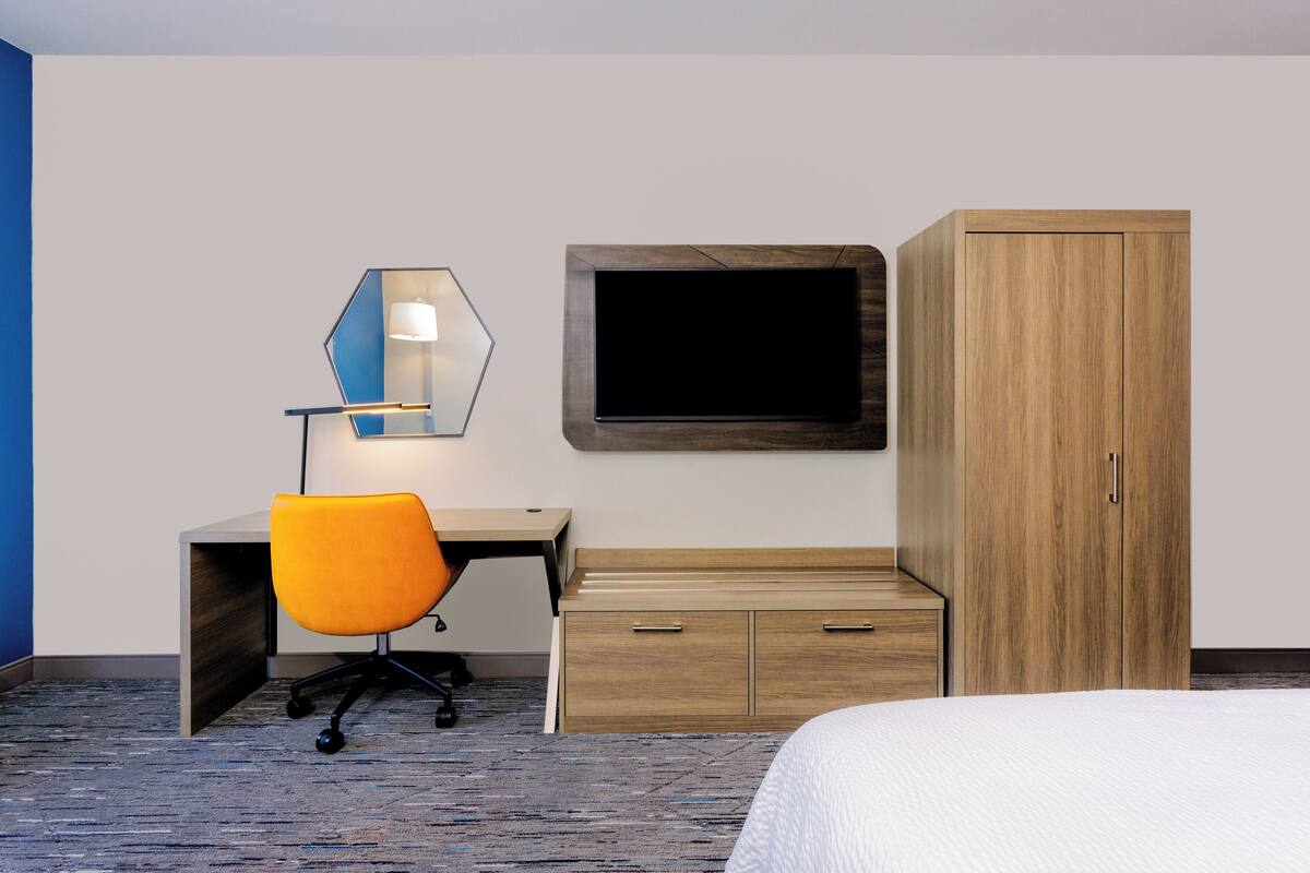 Hotellihuone, jossa on sänky, työpöytä tuolilla, televisio ja vaatekaappi.