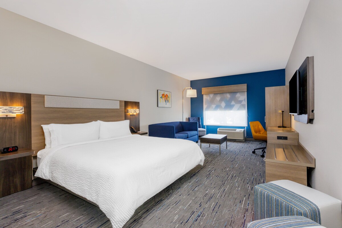 A modern hotel room with a large bed, a desk, a chair, and a TV.