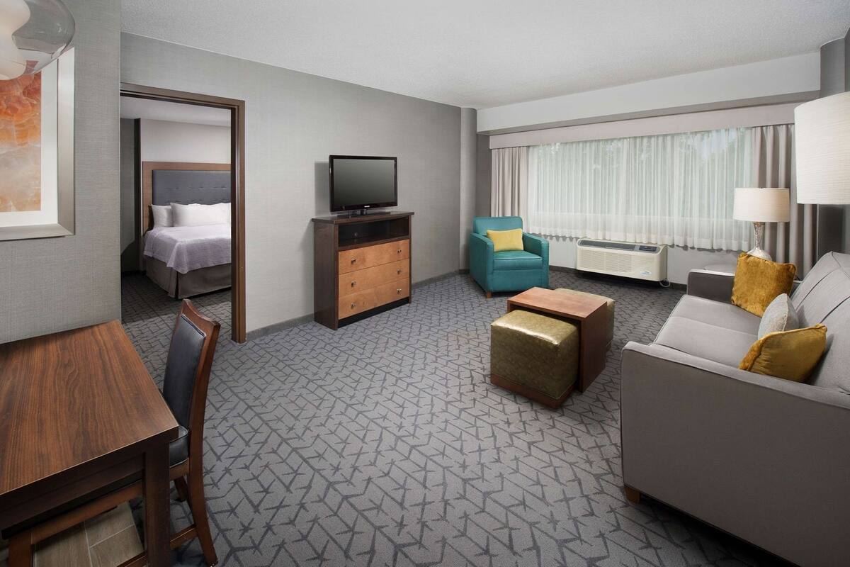 A hotel room with a bed, a TV, a sofa, a chair, a table, and a lamp.