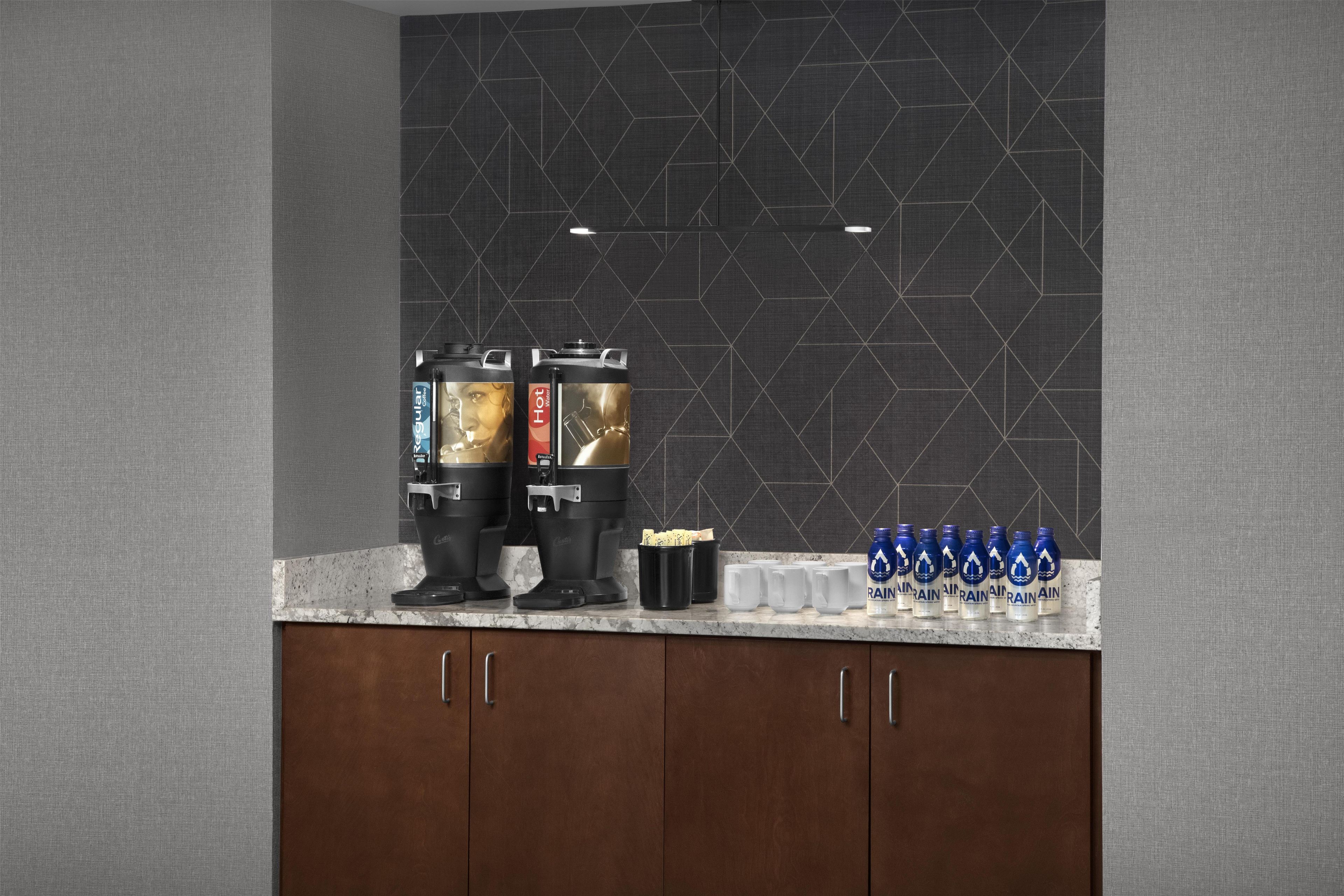 A kitchenette with two coffee makers, a coffee pot, and a row of water bottles on the counter.