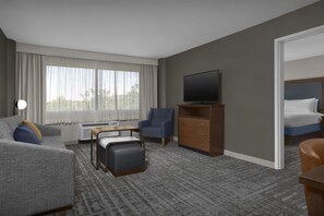 A hotel room with a sofa, armchair, ottoman, TV, dresser, and a bed. - Homewood Suites by Hilton Gaithersburg/ Washington, DC North (Gaithersburg)