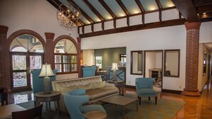 A spacious lobby with a high ceiling, exposed beams, and large windows with stained glass. There are several seating areas with sofas and armchairs, and a coffee table in the center. - The Flagler Inn (St. Augustine)