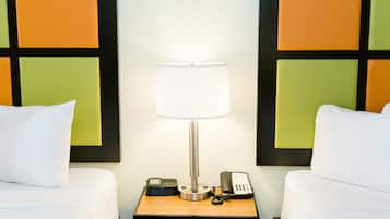 A hotel room with two beds, a bedside table with a lamp, a telephone, and a small device on the table.