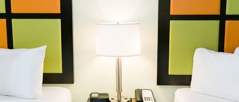 Et hotelværelse med to senge, et natbord med lampe, telefon og en lille enhed på bordet.
