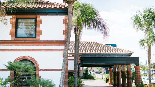 A building with a red brick facade, a tiled roof, and a covered entrance area with columns. - The Flagler Inn (St. Augustine)