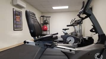 A stationary bike with a weight stack and a red medicine ball on a rack.