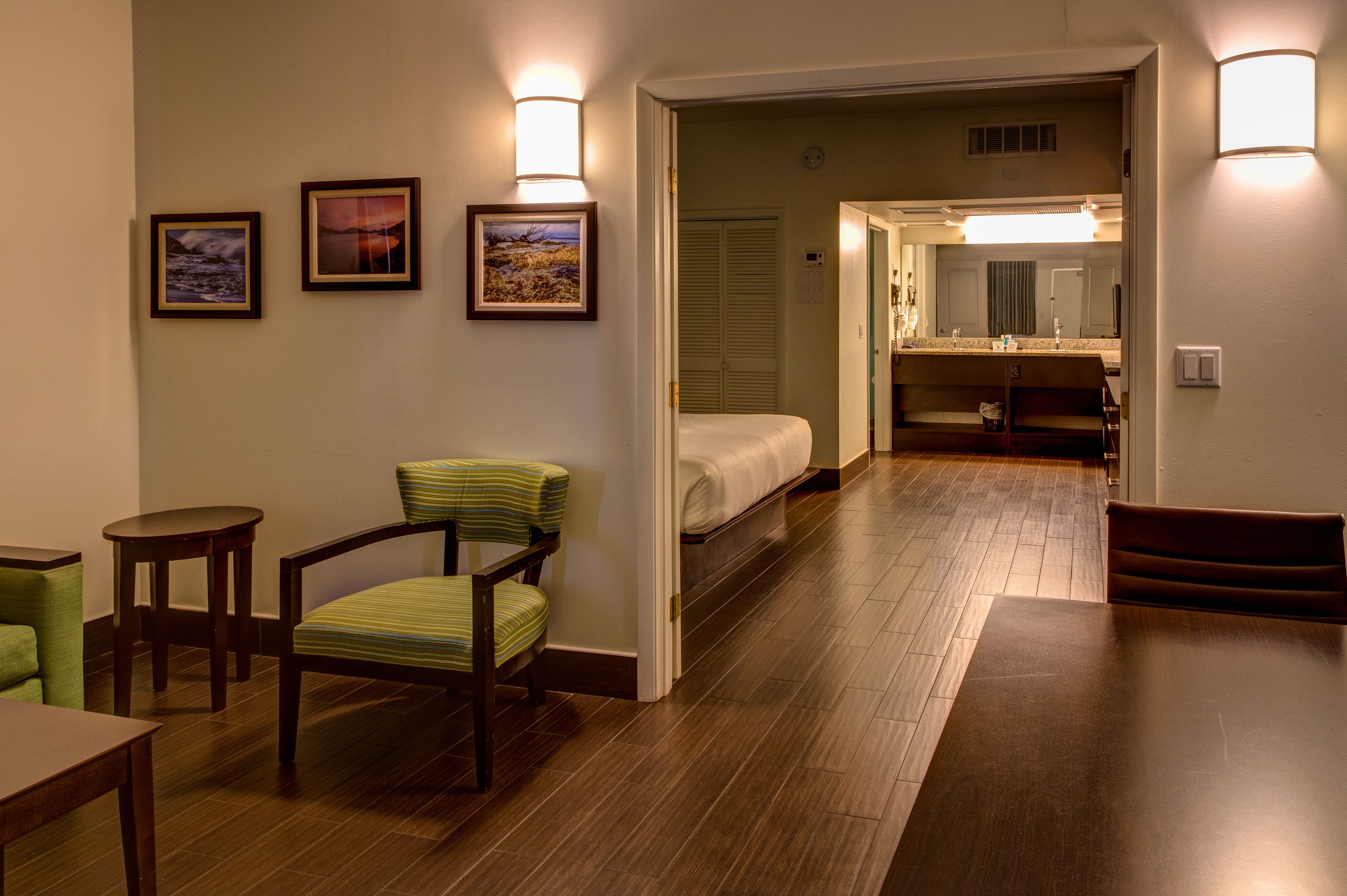 Quarto de hotel com cama, cadeira, mesa e banheiro com espelho e pia.
