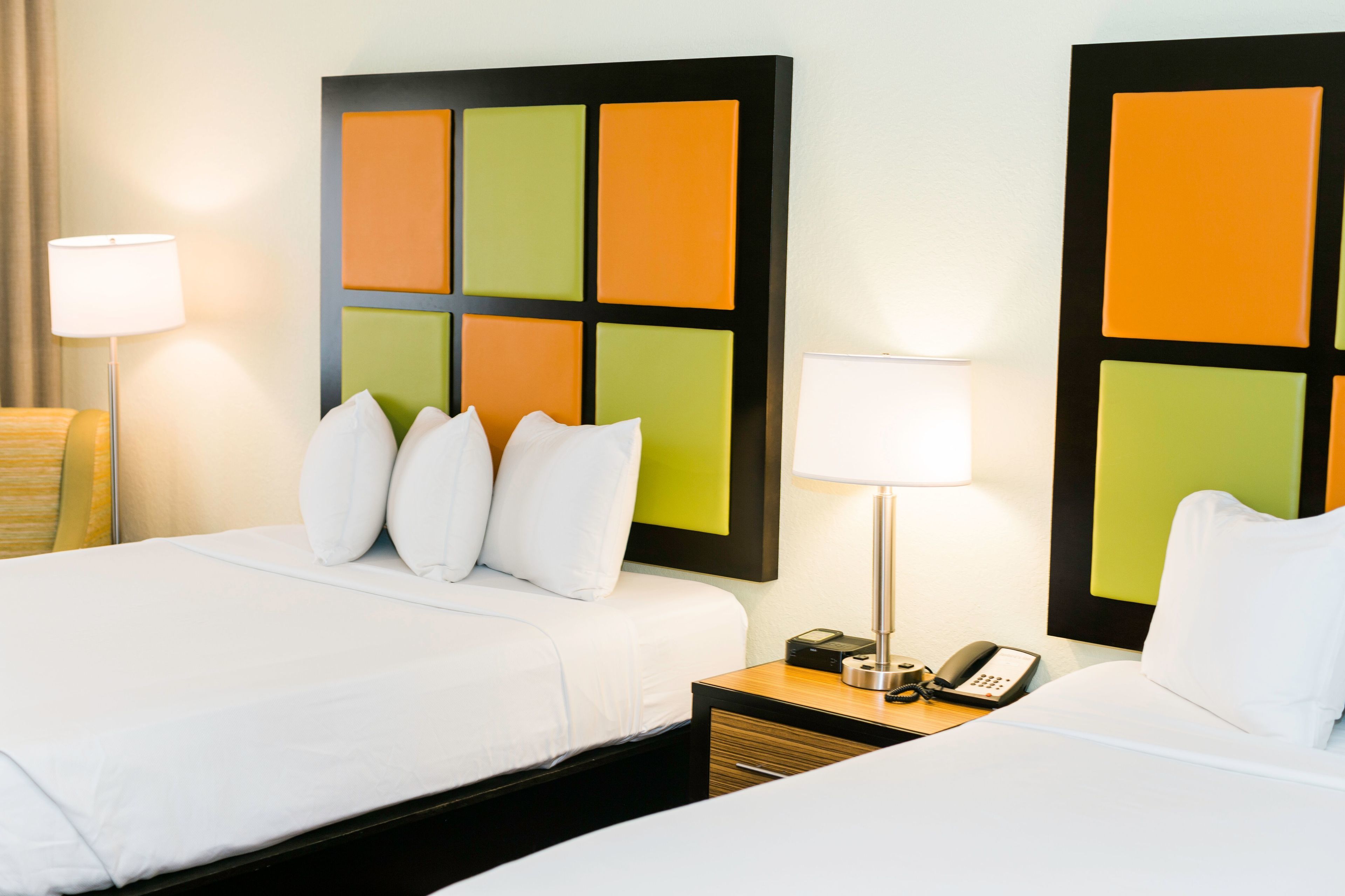 A hotel room with two beds, a nightstand with a lamp and phone, and a wall with a colorful panel design.