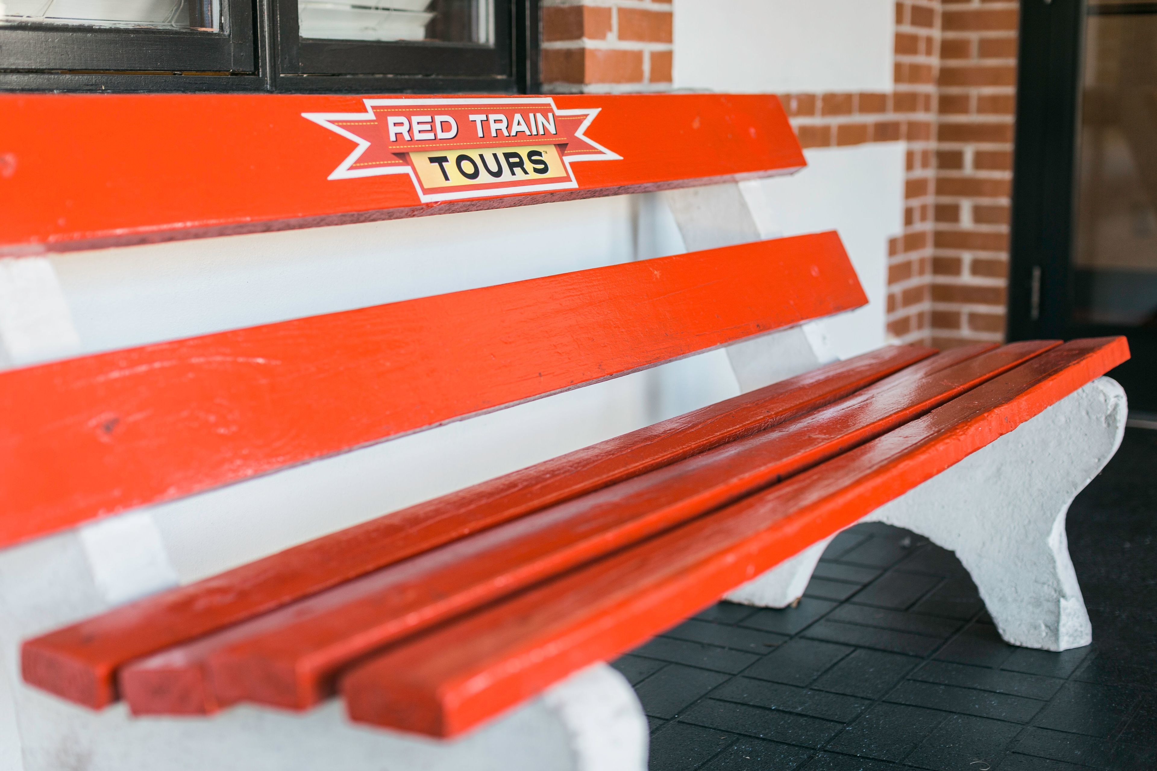 A red and white bench with a sign that reads "RED TRAIN TOURS".