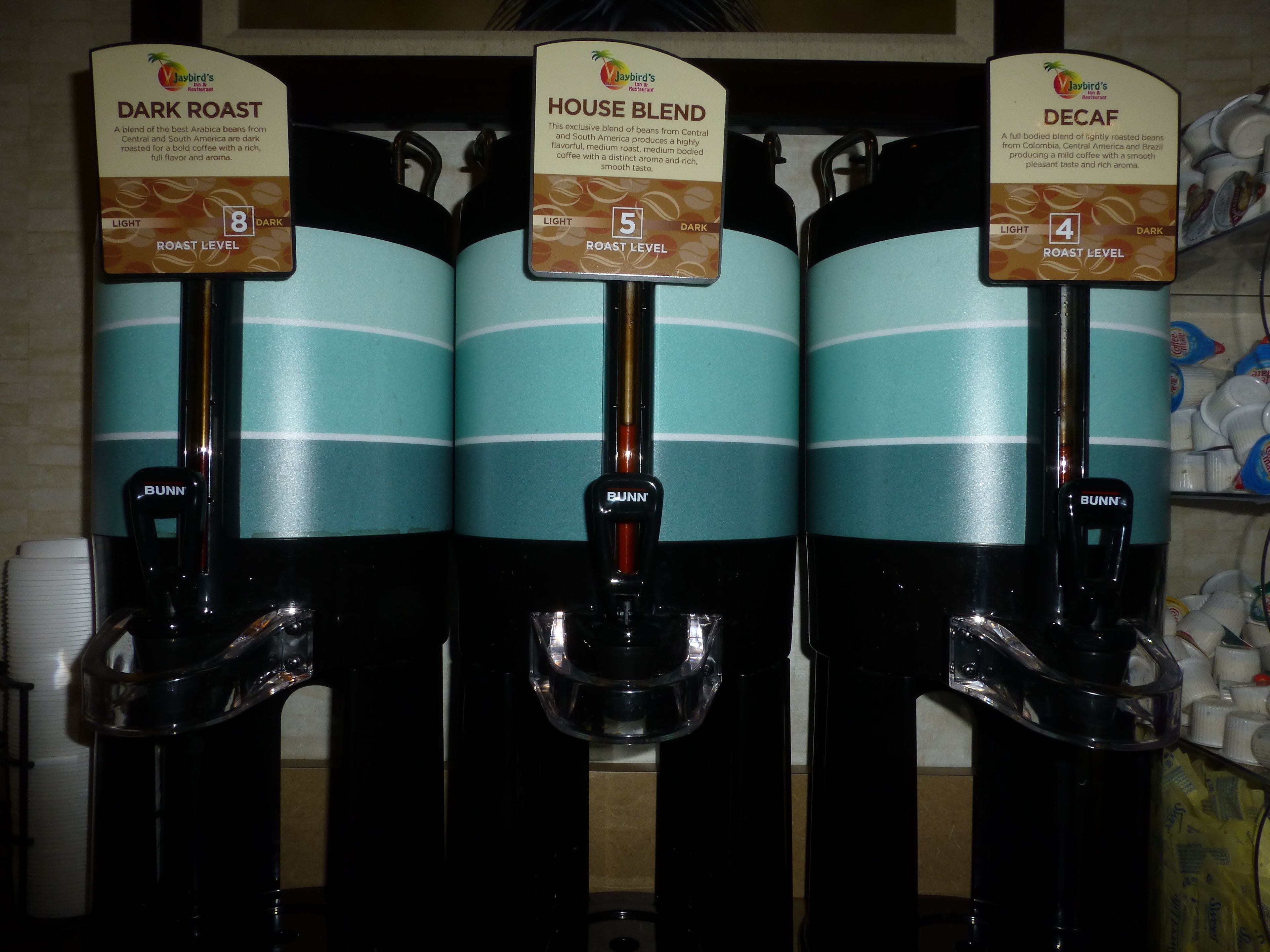 Tres dispensadores de café etiquetados con diferentes mezclas: Tueste Oscuro, Mezcla de la Casa y Descafeinado.