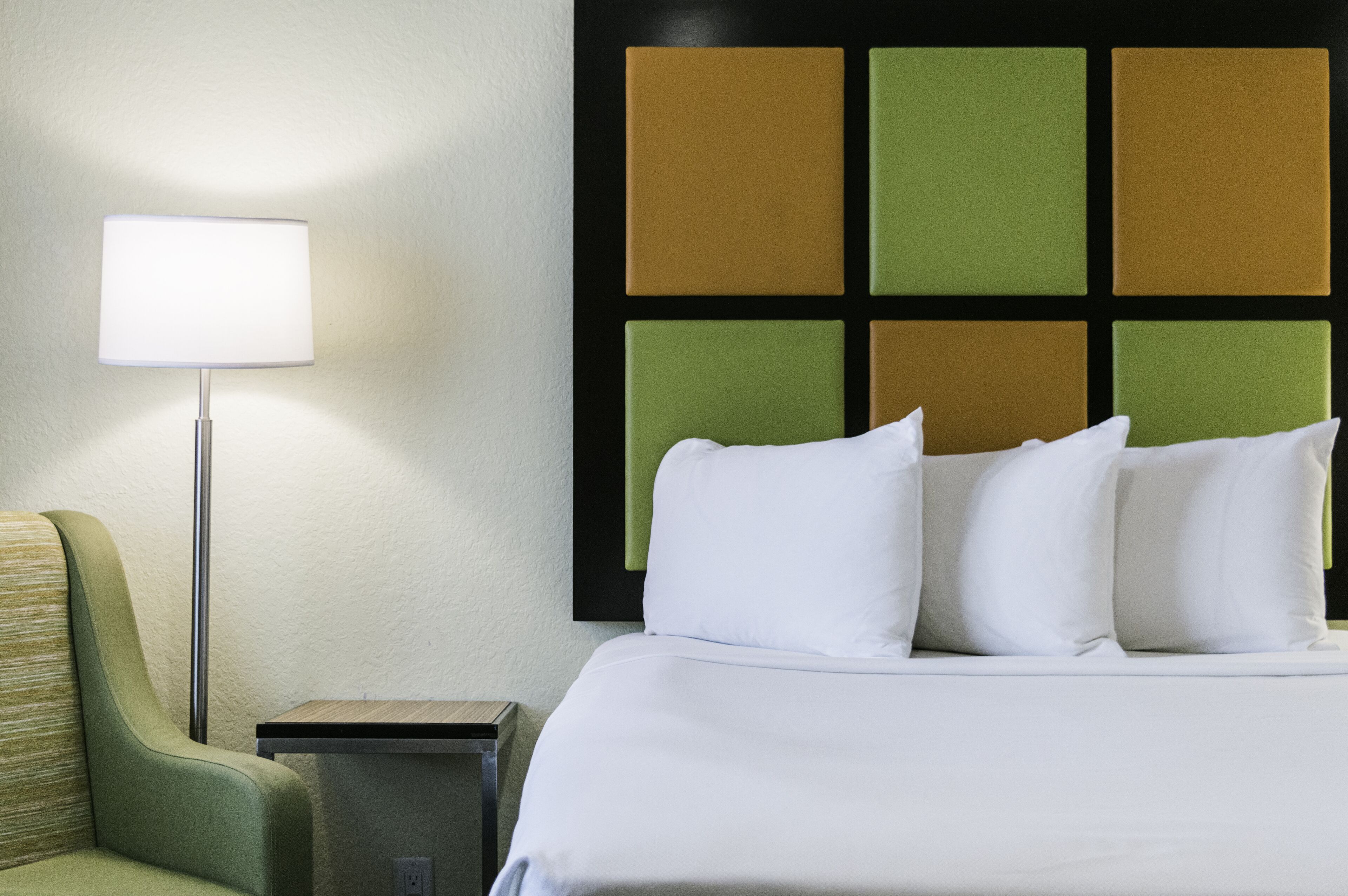Una habitación de hotel con cama, sillón, mesita de noche y pared con diseño geométrico.