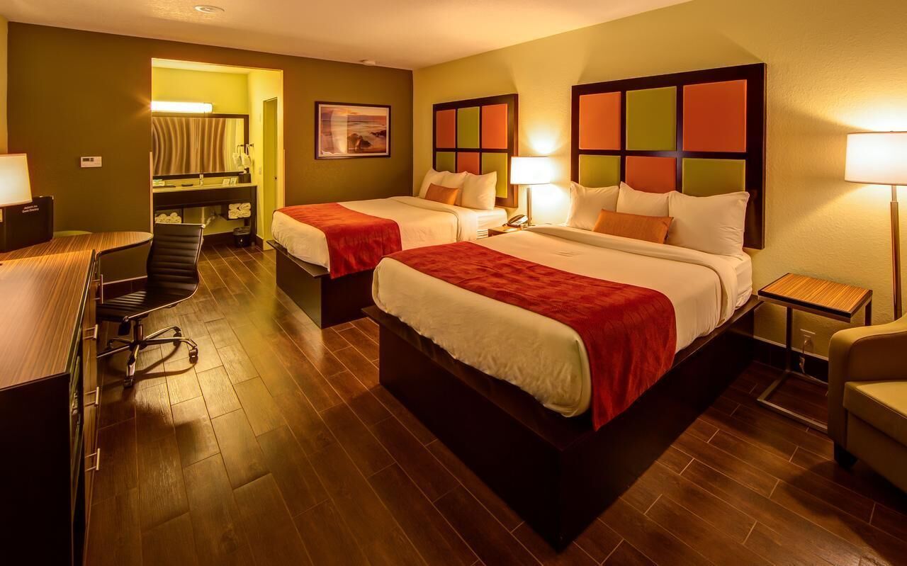 A hotel room with two beds, a desk, a chair, and a bathroom visible through an open door.