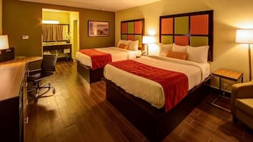 A hotel room with two beds, a desk, a chair, and a bathroom visible through an open door.