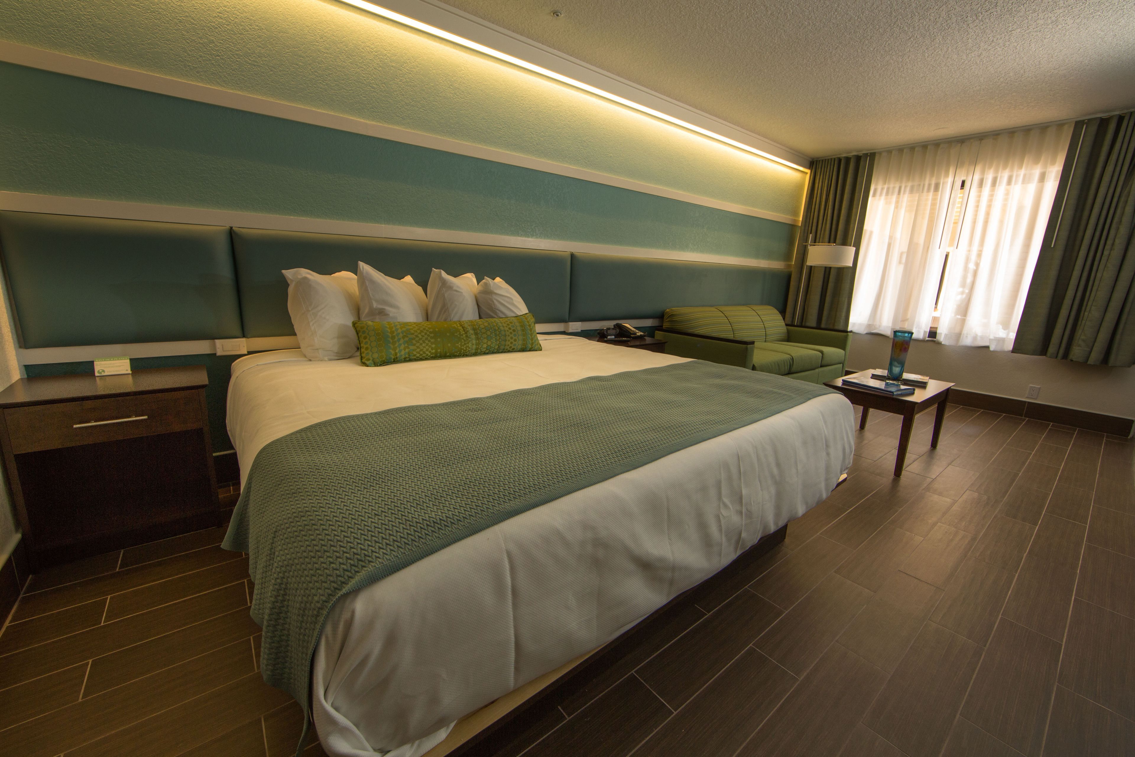A hotel room with a large bed, a green sofa, a nightstand, and a lamp.