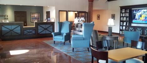 A lobby with a reception desk, seating area, and a television displaying sports.