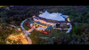 An aerial view of a large, uniquely shaped building surrounded by dense forest, with a curved pathway leading to it. - The Flagler Inn (St. Augustine)