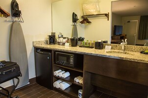 Un bagno d'albergo con un piano di lavoro in granito, un forno a microonde, una macchina da caffè e asciugamani sugli scaffali.