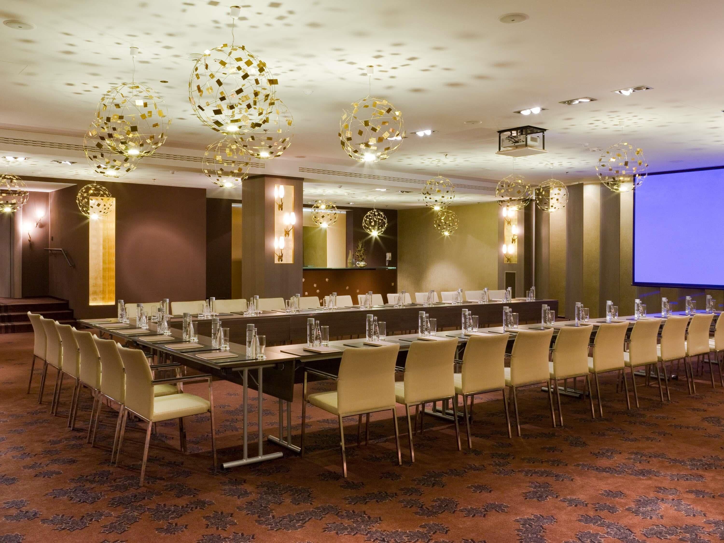 Un salón de conferencias con una larga mesa, sillas y una pantalla para proyector.