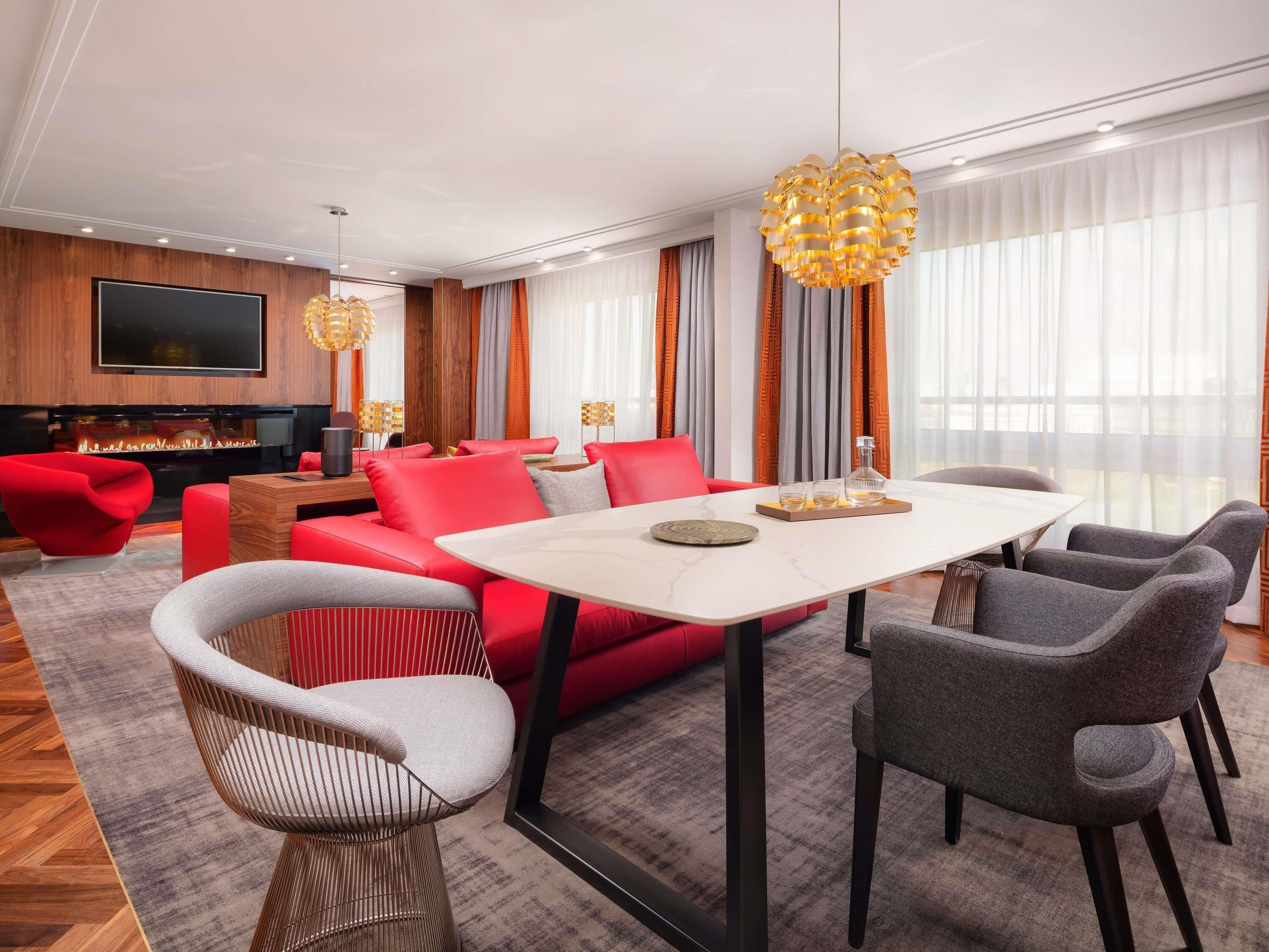 A modern living room with a red sofa, grey chairs, a white table, and a fireplace.