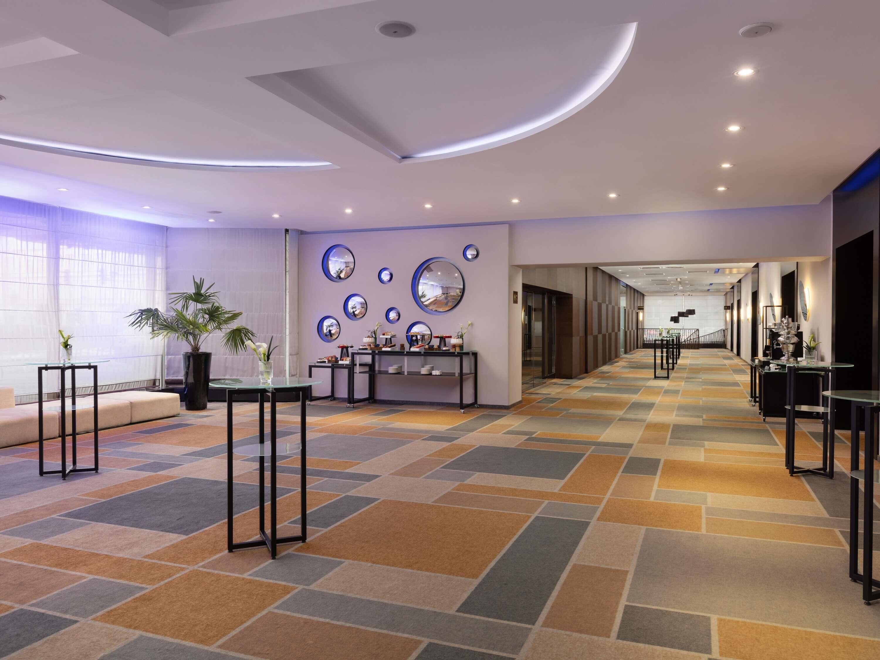 A modern hotel lobby with a check-in desk, seating area, and decorative mirrors.