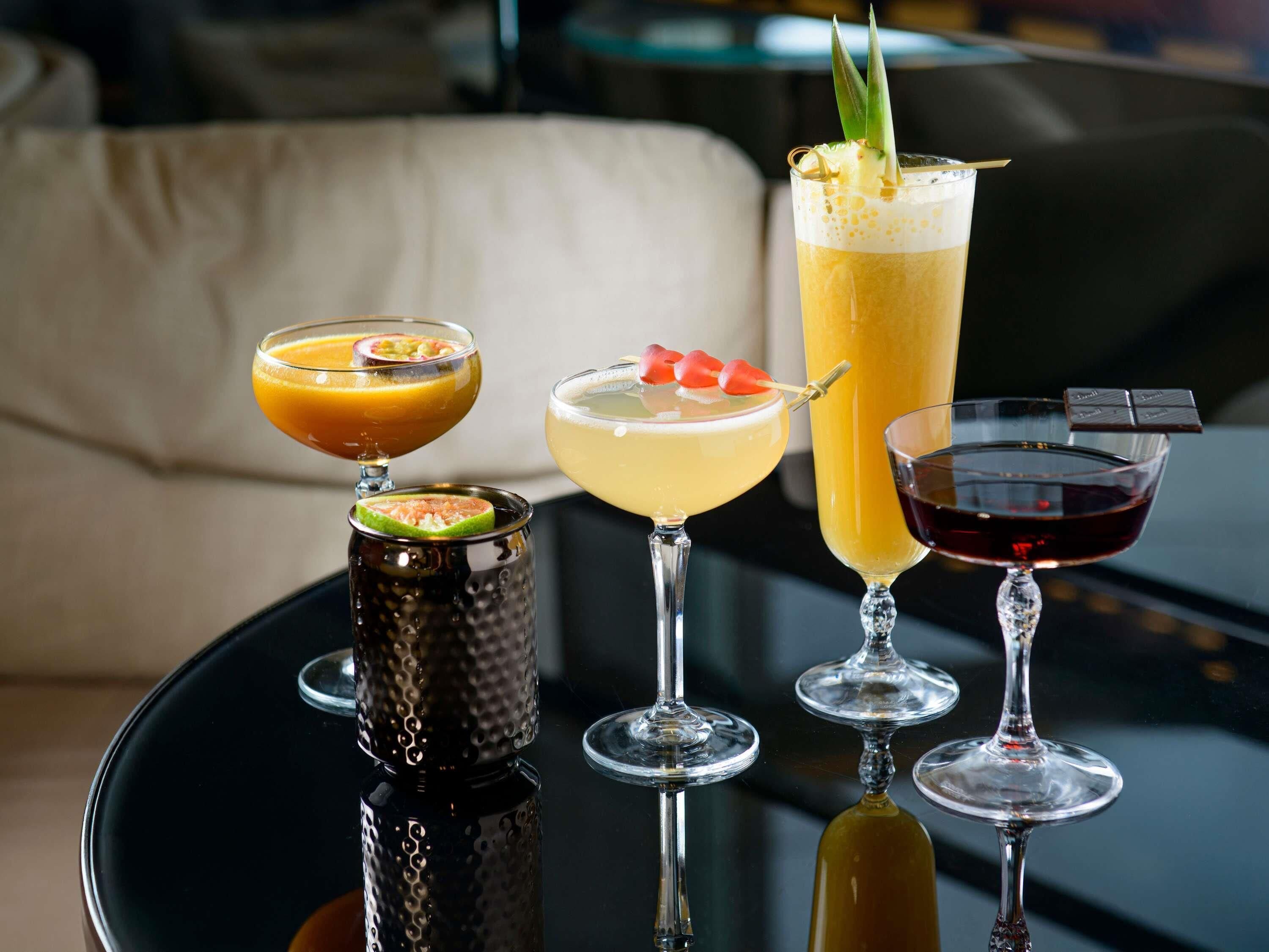 Quatre cocktails sur une table noire, avec un canapé en arrière-plan.