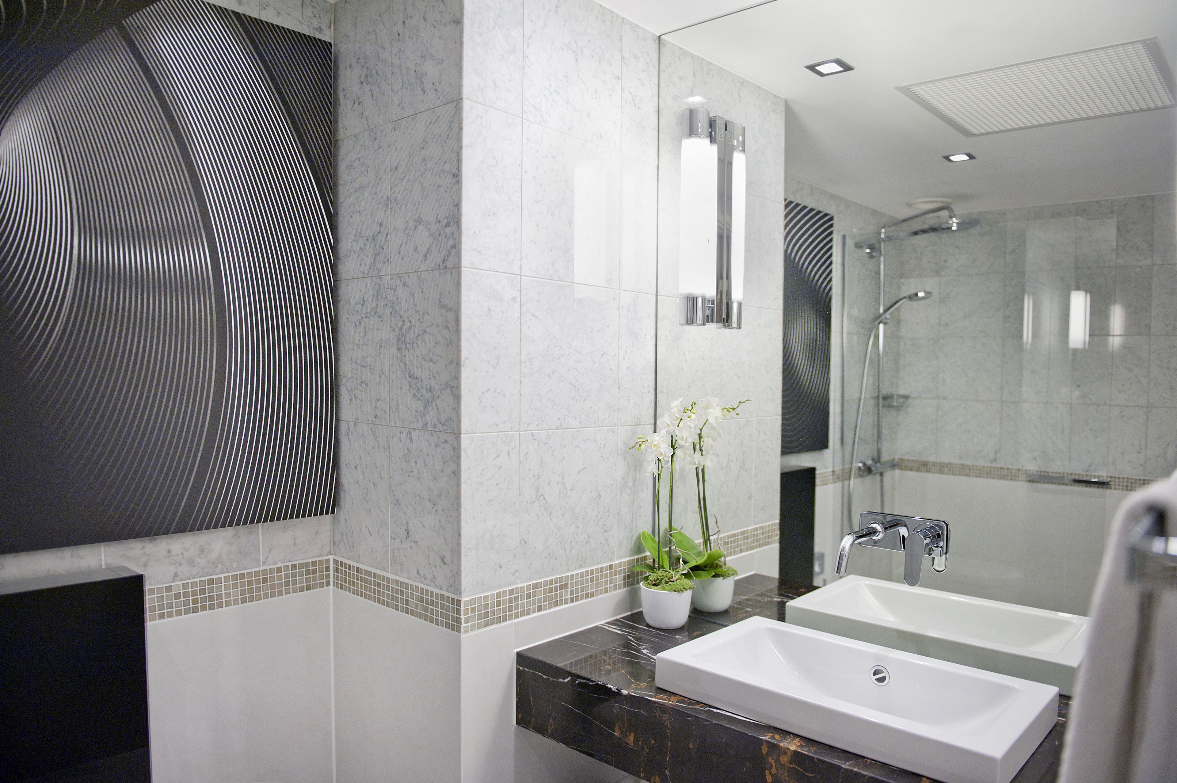 A modern bathroom with two sinks, a glass shower enclosure, and decorative plants.