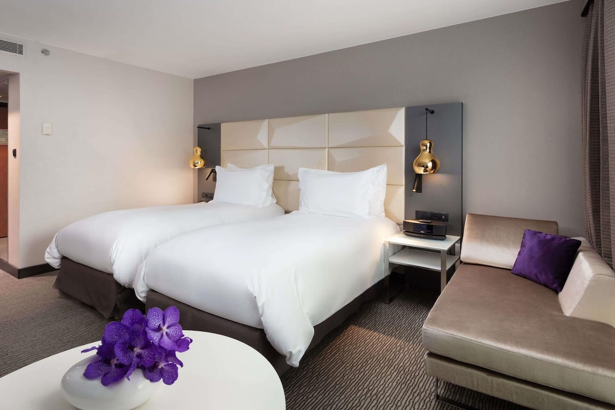 A hotel room with a large bed, two bedside tables, a sofa, and a small table with a purple orchid.