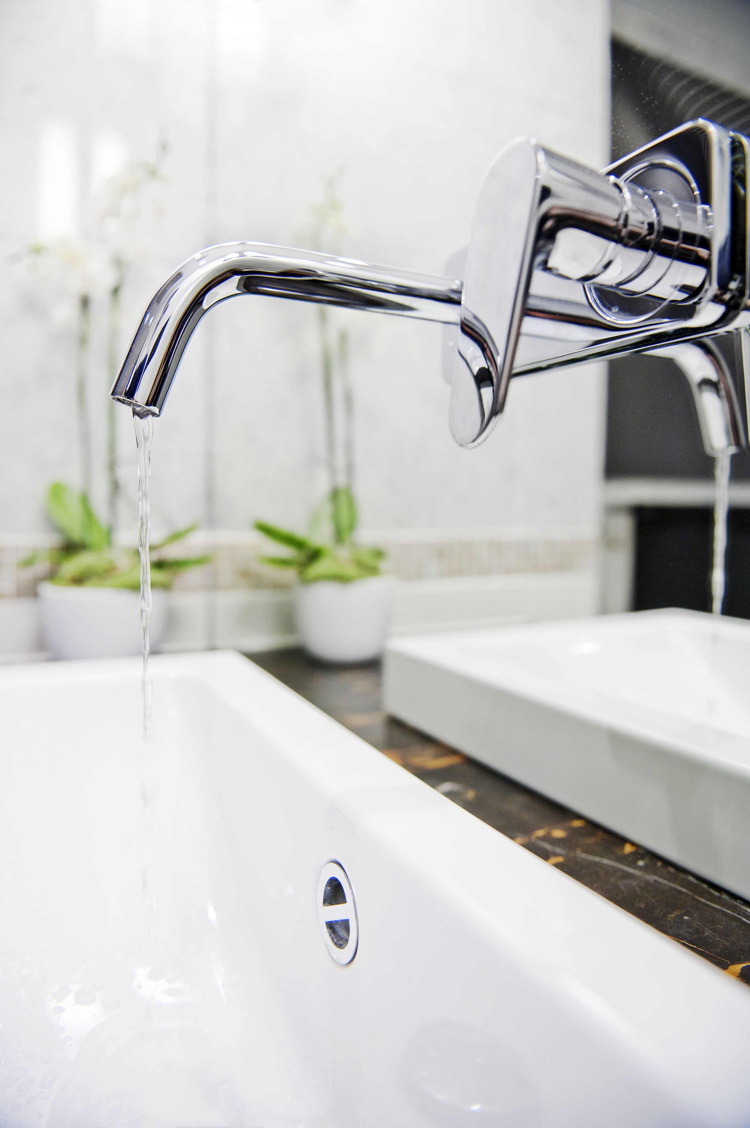 A modern bathroom with a chrome faucet, a white sink, and potted plants in the background.
