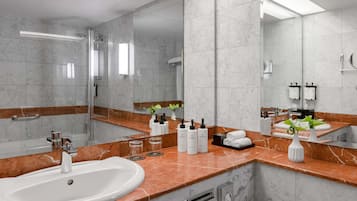 A modern bathroom with a marble sink, large mirror, and toiletries on the counter.
