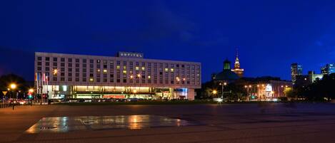 A hotel with a modern facade, a prominent tower, and a large open plaza.