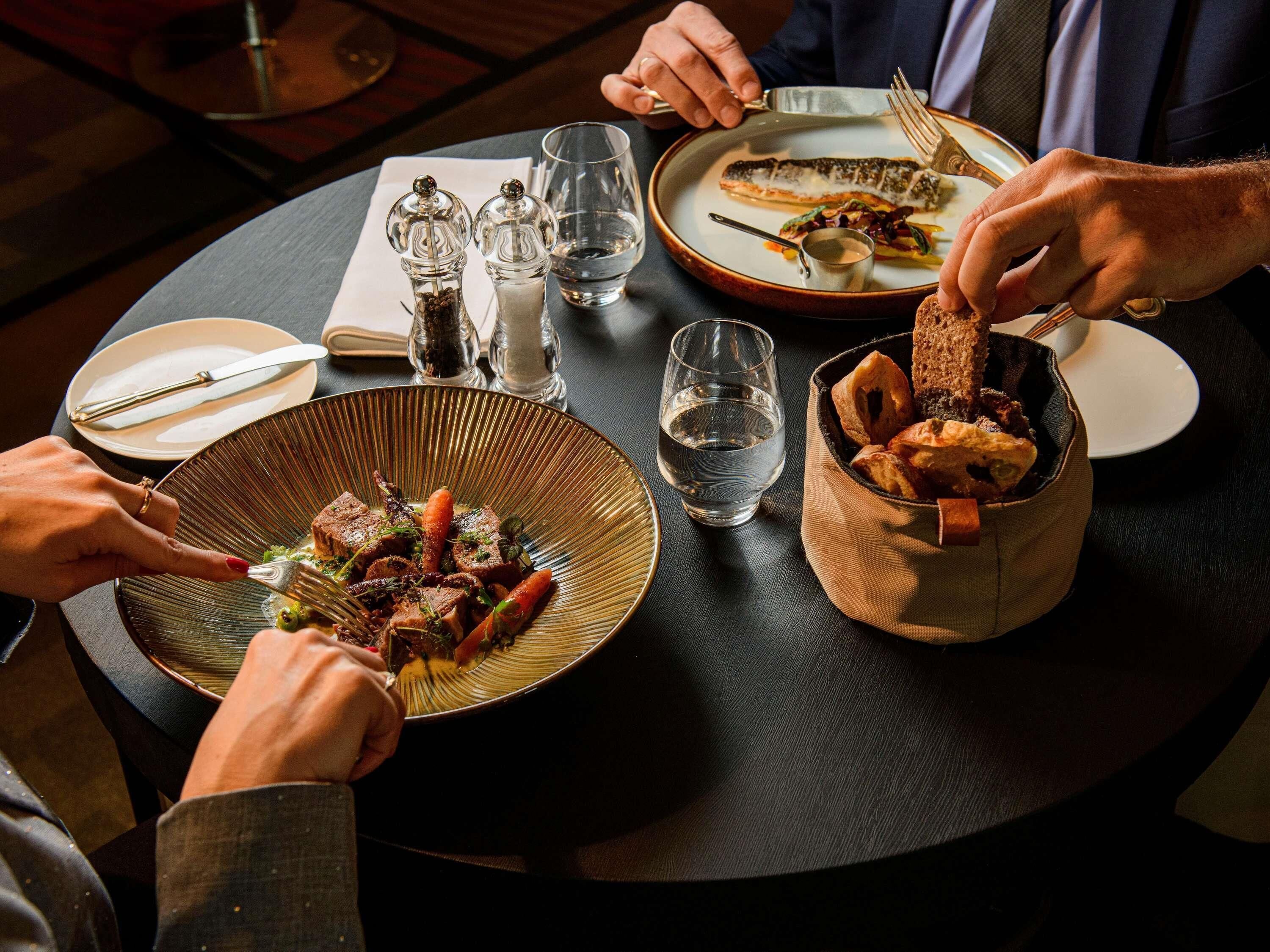 A dining table with plates of food, glasses of water, and salt and pepper shakers.