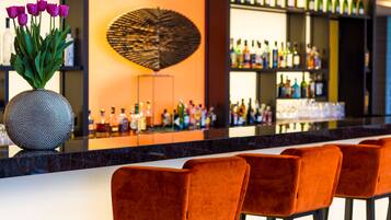 A bar area with a long counter, multiple bottles of alcohol, and a decorative wall piece.