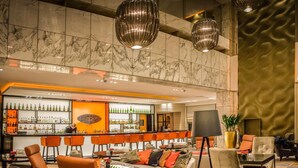 A modern bar area with a marble wall, a variety of bottles, and orange chairs. - Sofitel Warsaw Victoria (Warsaw)